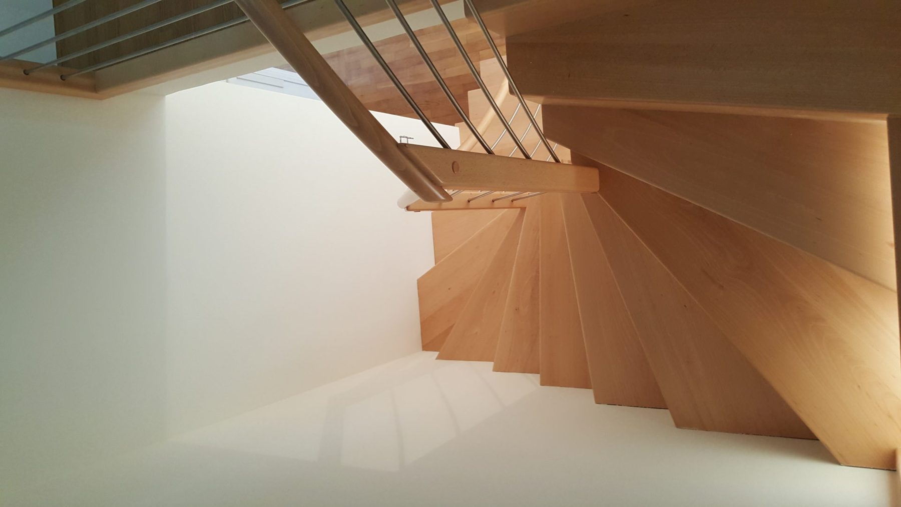 Escalier en bois clair avec garde-corps à câbles inox, vu depuis l’étage
