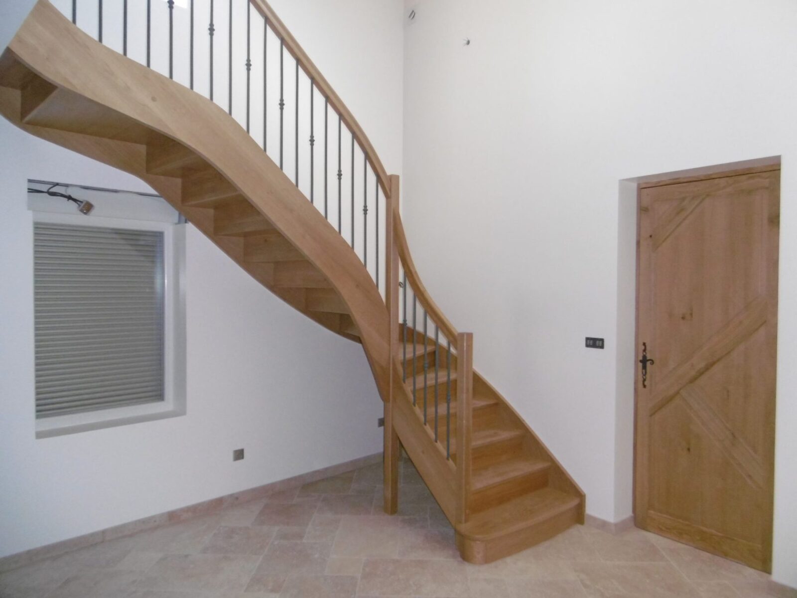 Escalier bois débillardé avec balustres en fer peint, dans une entrée lumineuse
